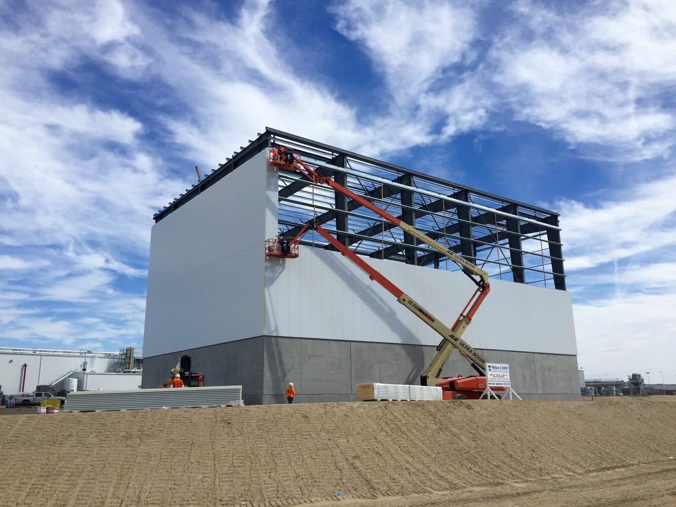 Steel framing and wall panels going up on a pre-engineered building, with crews on boom lifts